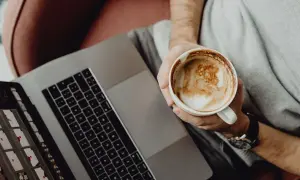 Osoba z kawą na laptopie, ucząca się Mac OS dla początkujących.