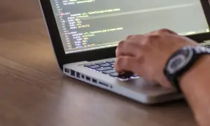 Dłoń programisty pisze kod na laptopie. Zastanawiasz się, ile zarabia programista po studiach?