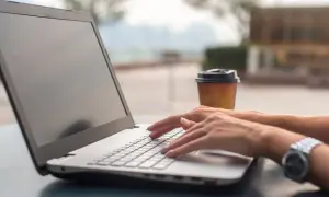 Kobieta pisze na laptopie, zastanawiając się, co zainstalować na nowym komputerze. Obok stoi kubek kawy.