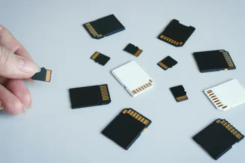 Różne karty pamięci, w tym micro SD, leżą na jasnym tle. Jedna karta jest trzymana w palcach. To jest karta pamięci.