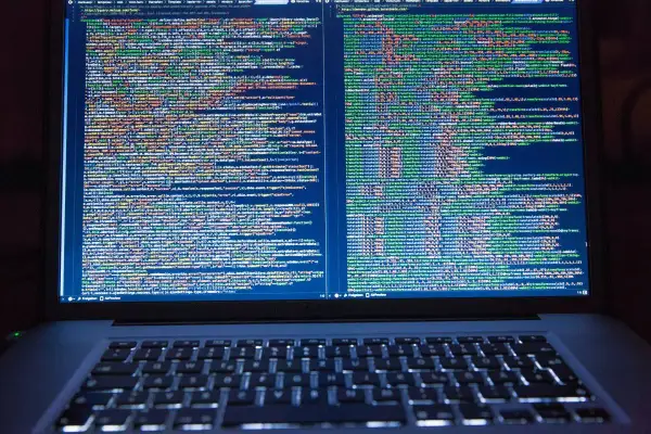 Programista pracuje nad kodem. Na ekranie laptopa widać wiele linii kodu, co pokazuje, co robi programista.